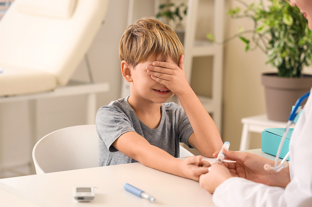 Scared little diabetic boy with doctor using lancet pen at table in clinic